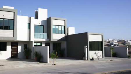 Casa de dos niveles con balcones de vidrio, mezcla de tonos grises y blancos y iluminación natural